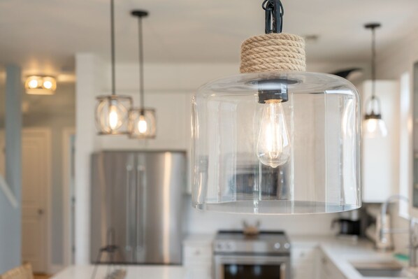 A modern kitchen with stainless steel appliances, pendant lights, and a clear glass light fixture.