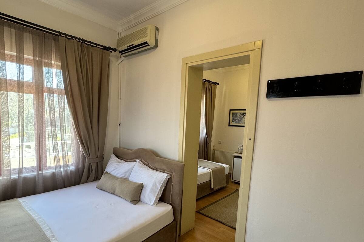 Une chambre à coucher avec un lit, des rideaux, un appareil de climatisation, un miroir et une petite table avec des articles de toilette.