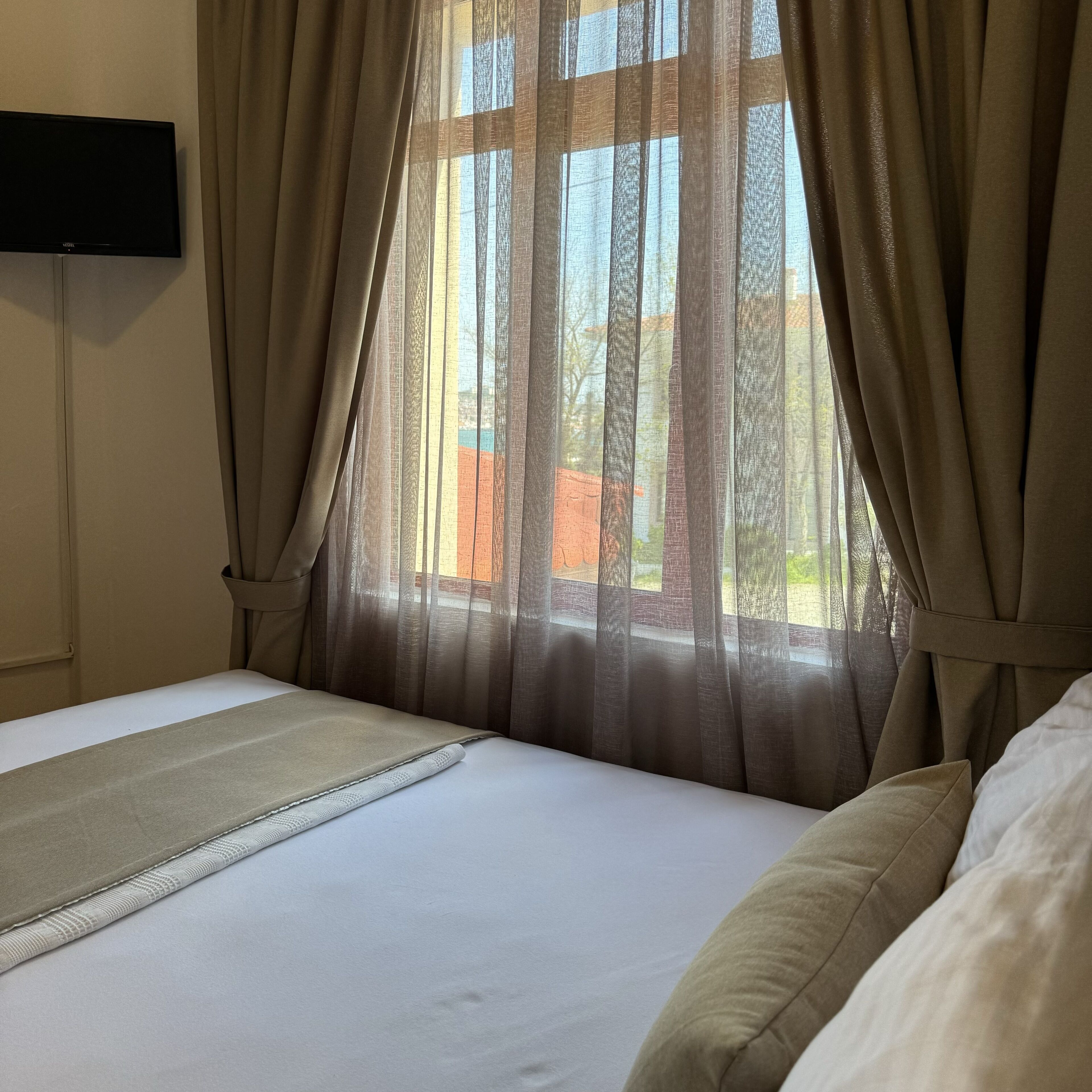 Ett hotellrum med en säng, beige gardiner och utsikt över omgivningarna.