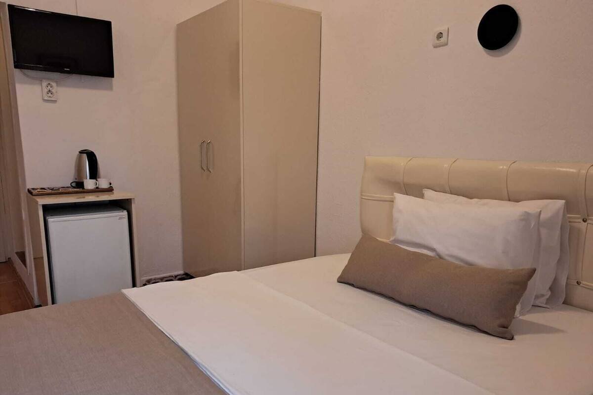 Une chambre comprenant un lit, une armoire, un petit bureau avec une bouilloire et un téléviseur fixé au mur.