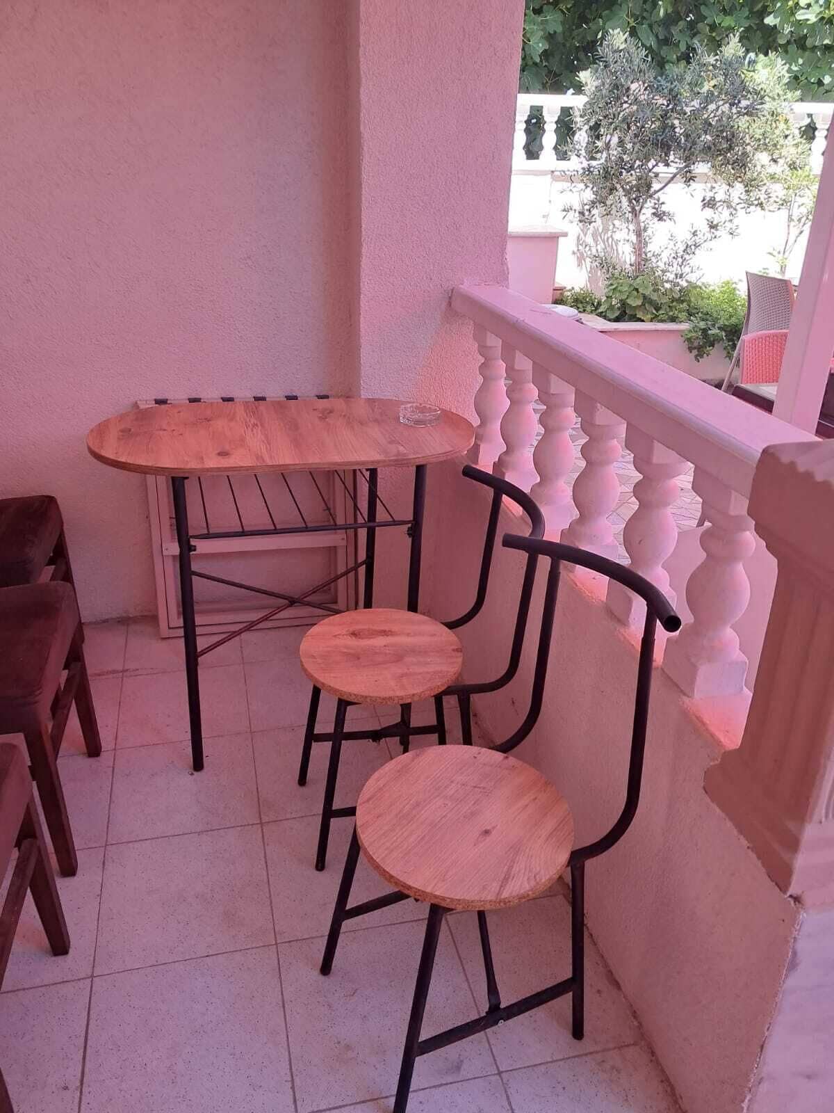 Een klein terras buiten met een ronde tafel en vier stoelen, een witte balustrade en zicht op groen in de verte.