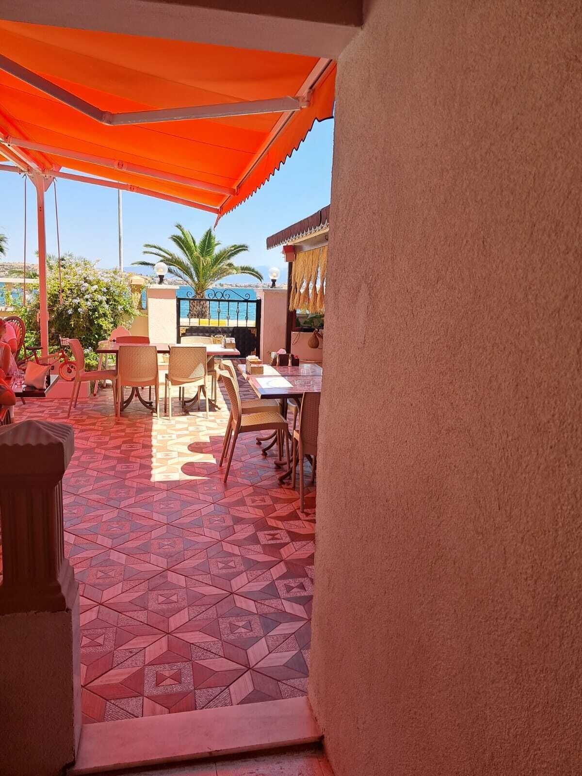 An outdoor seating area with tables and chairs, a patterned floor, and a view of the sea.