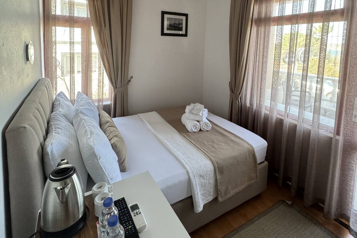 Une chambre d’hôtel avec un lit, une table de chevet avec une bouilloire, une télécommande et un tableau au mur.