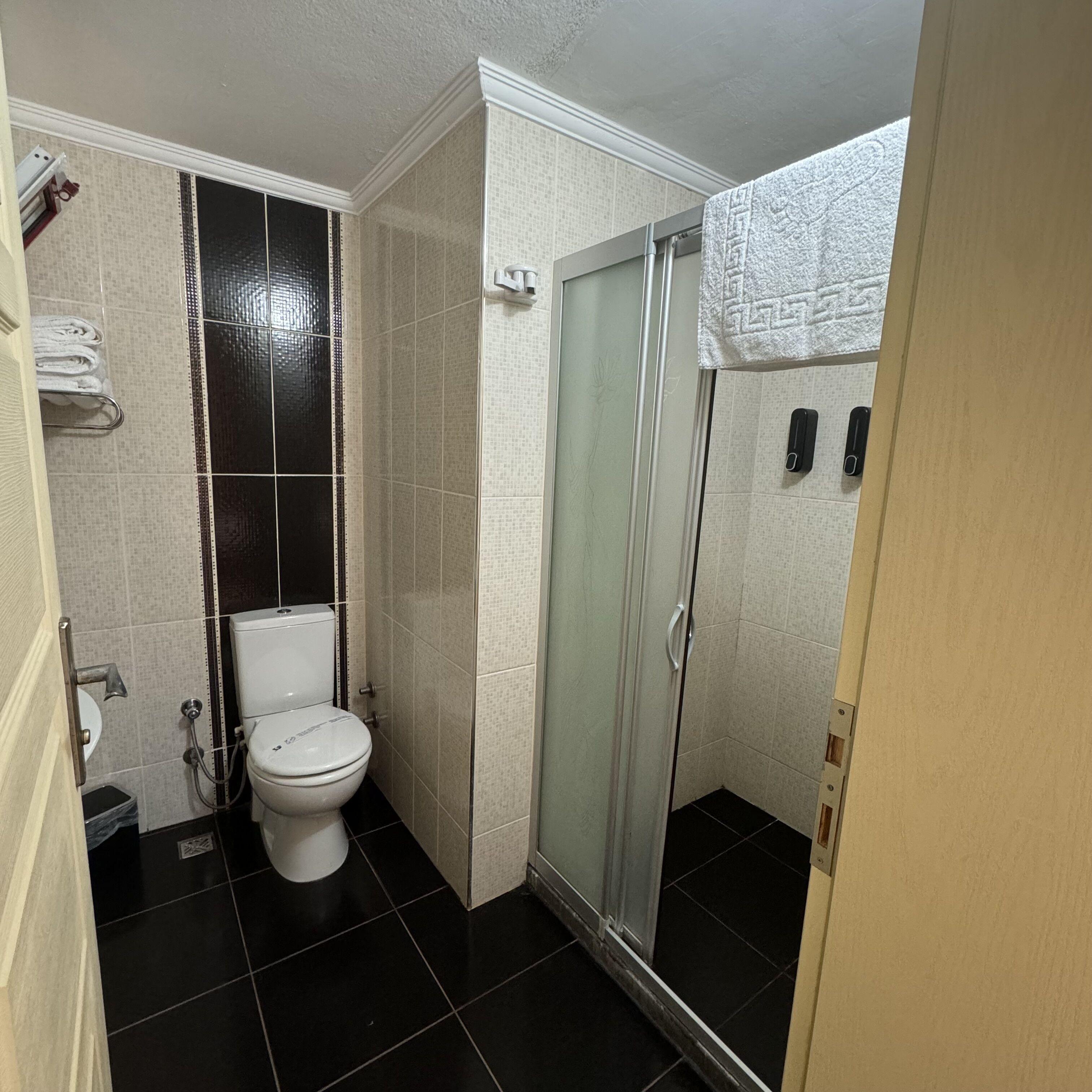 Un baño pequeño con inodoro, cabina de ducha y un perchero para toallas.