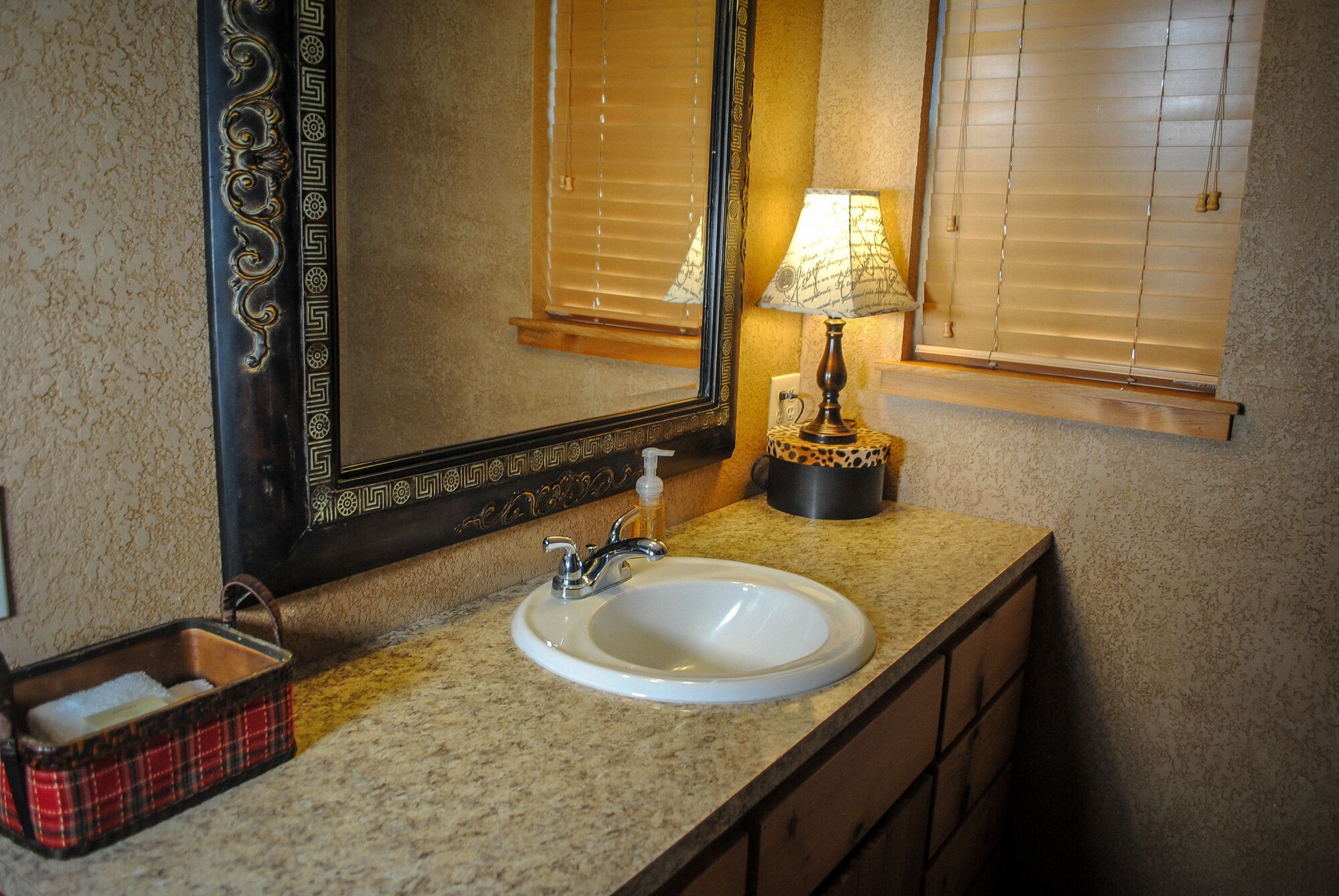 Une salle de bain avec un lavabo blanc, un miroir doté d’un cadre décoratif, un porte-serviettes et une lampe posée sur le comptoir.