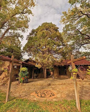 Un edificio rústico de piedra con un gran árbol en el centro, rodeado de construcciones de madera y un patio de piedra.