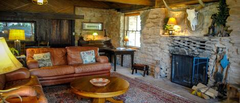 A rustic interior with a stone fireplace, leather sofa, and a wooden table.