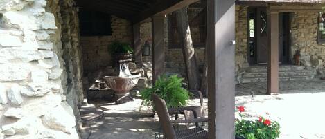 A stone building with a covered patio area featuring a large urn, a bench, and potted plants.
