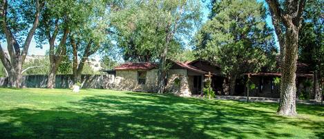 A stone house with a red roof, surrounded by a well-maintained lawn and tall trees.
