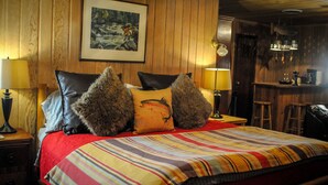 Een gezellige kamer met een houten wand, een bed met gestreepte beddengoed en een ingelijste foto boven het bed.