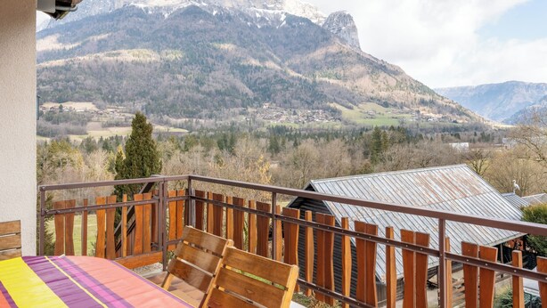 En balkon med trægelænder og udsigt over et bjerrelandskab.