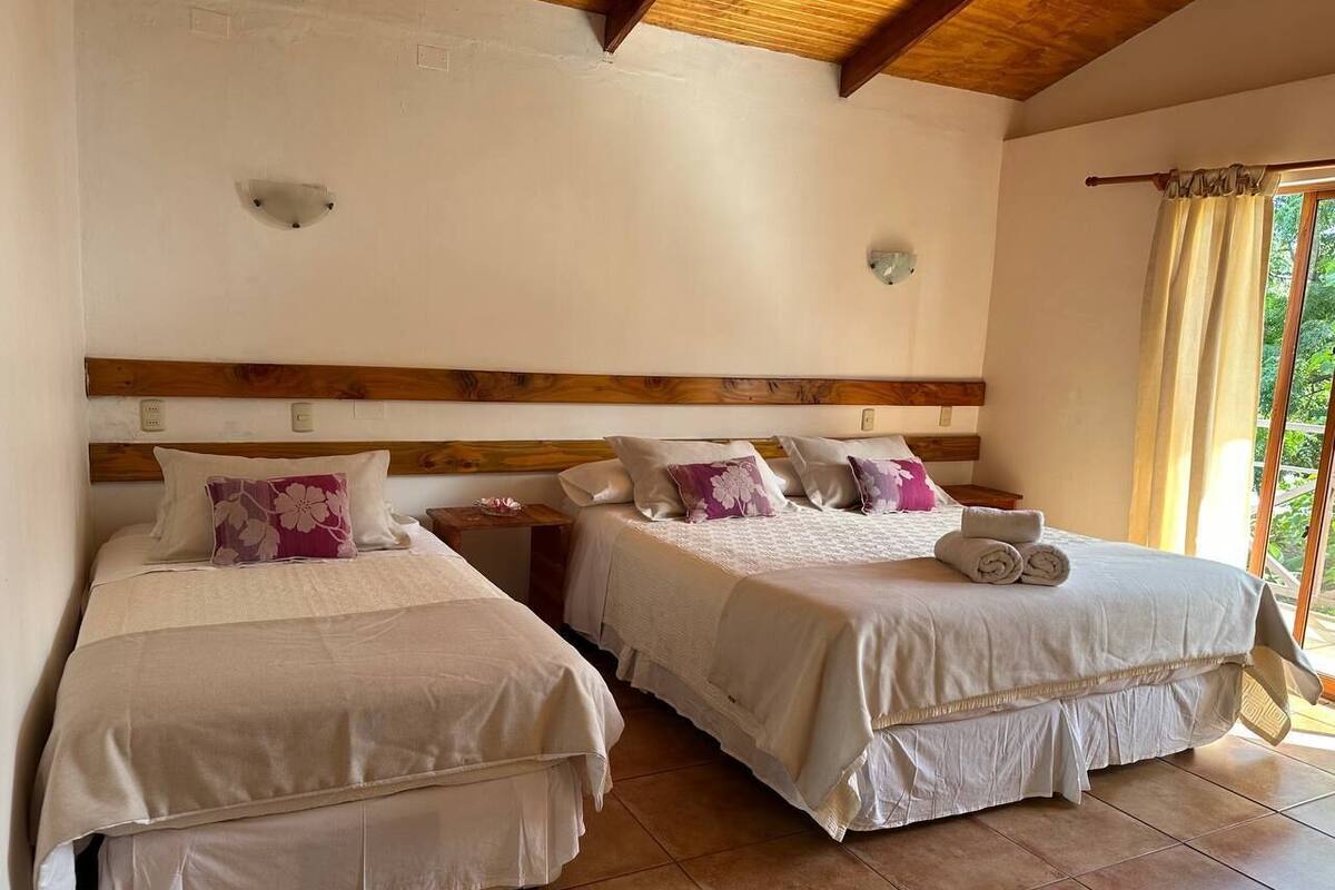 A bedroom with two beds, wooden headboards, and a large window with curtains.