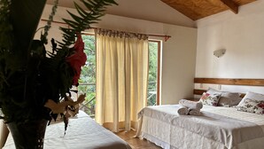 Un dormitorio con dos camas, techo de madera, ventana con cortinas y una planta en maceta.