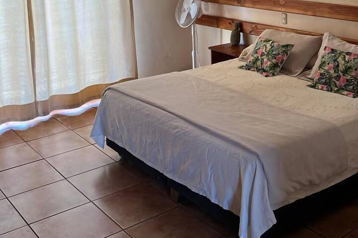 A bedroom with a bed, a ceiling fan, a window with curtains, and a wooden ceiling.