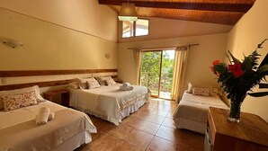 Una habitación de hotel con tres camas individuales, techo de madera y un ventanal con cortinas.