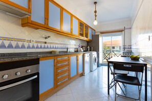 Una cocina con armarios de madera, horno empotrado, lavadora y comedor con mesa y sillas.