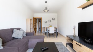 Un saló modern amb un sofà, una taula de centre, una televisió i una zona de menjador al fons.
