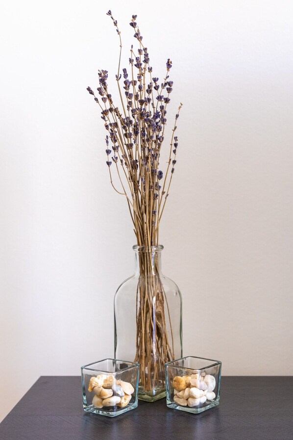 Un jarrón de cristal transparente con ramas de lavanda seca y dos pequeños recipientes de vidrio con piedras sobre una superficie oscura.