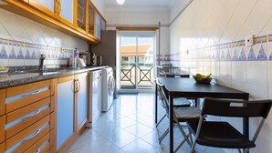 Una cuina amb armaris de fusta, una rentadora i una zona de menjador amb taula i cadires.