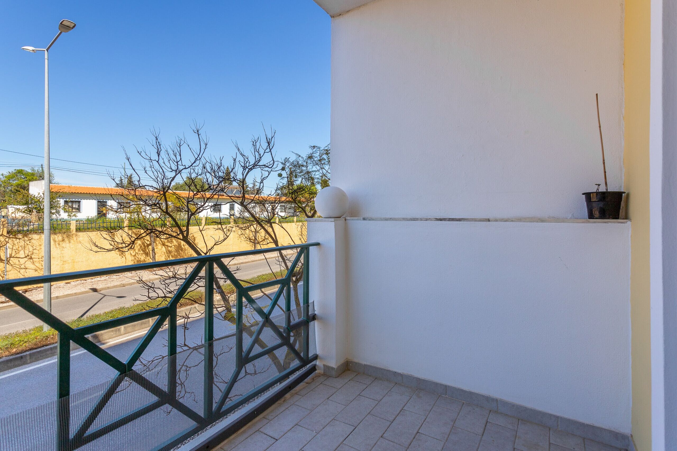 A balcony with a metal railing, a potted plant, and a clear view of a street and buildings.