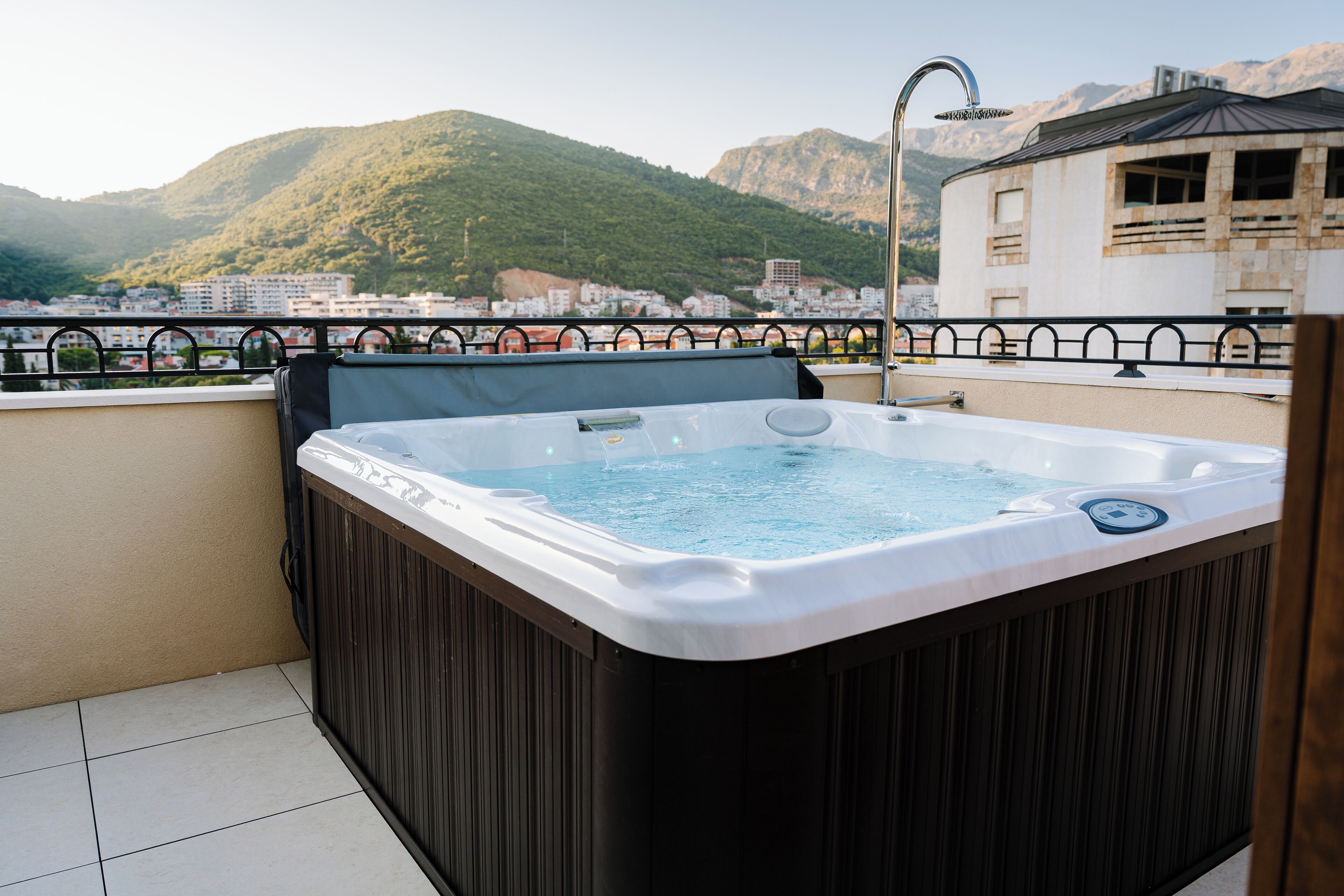 A hot tub on a balcony with a view of mountains and a cityscape.