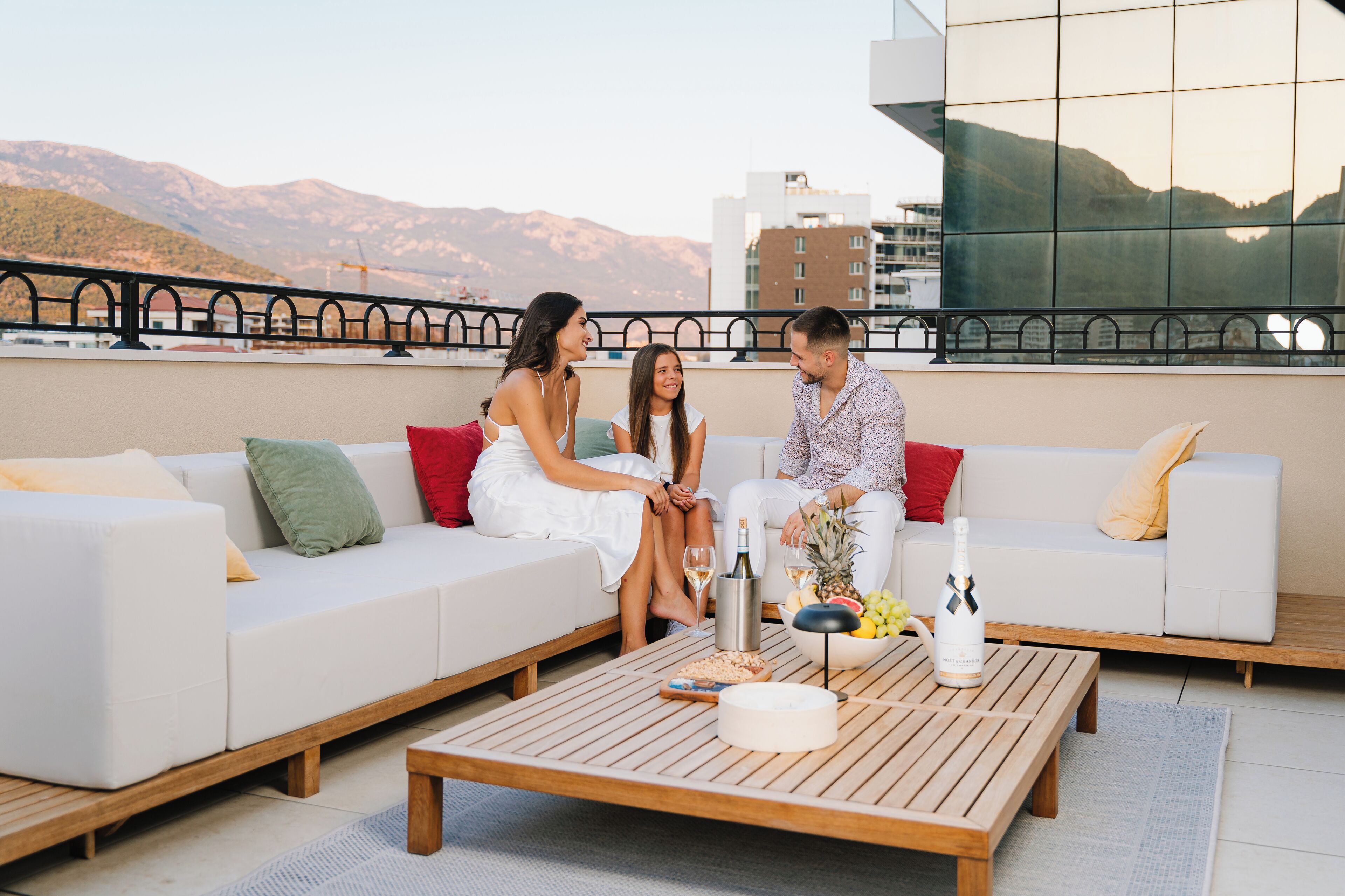 A rooftop terrace with a white sofa, wooden coffee table, and a cityscape view.
