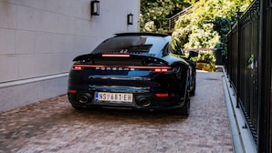 Un Porsche negro estacionado en un camino de ladrillo junto a un edificio blanco con luces empotradas negras.