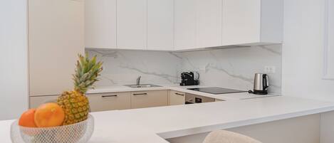 A modern kitchen with white cabinetry, a marble backsplash, and a built-in island with a bowl of fruit.