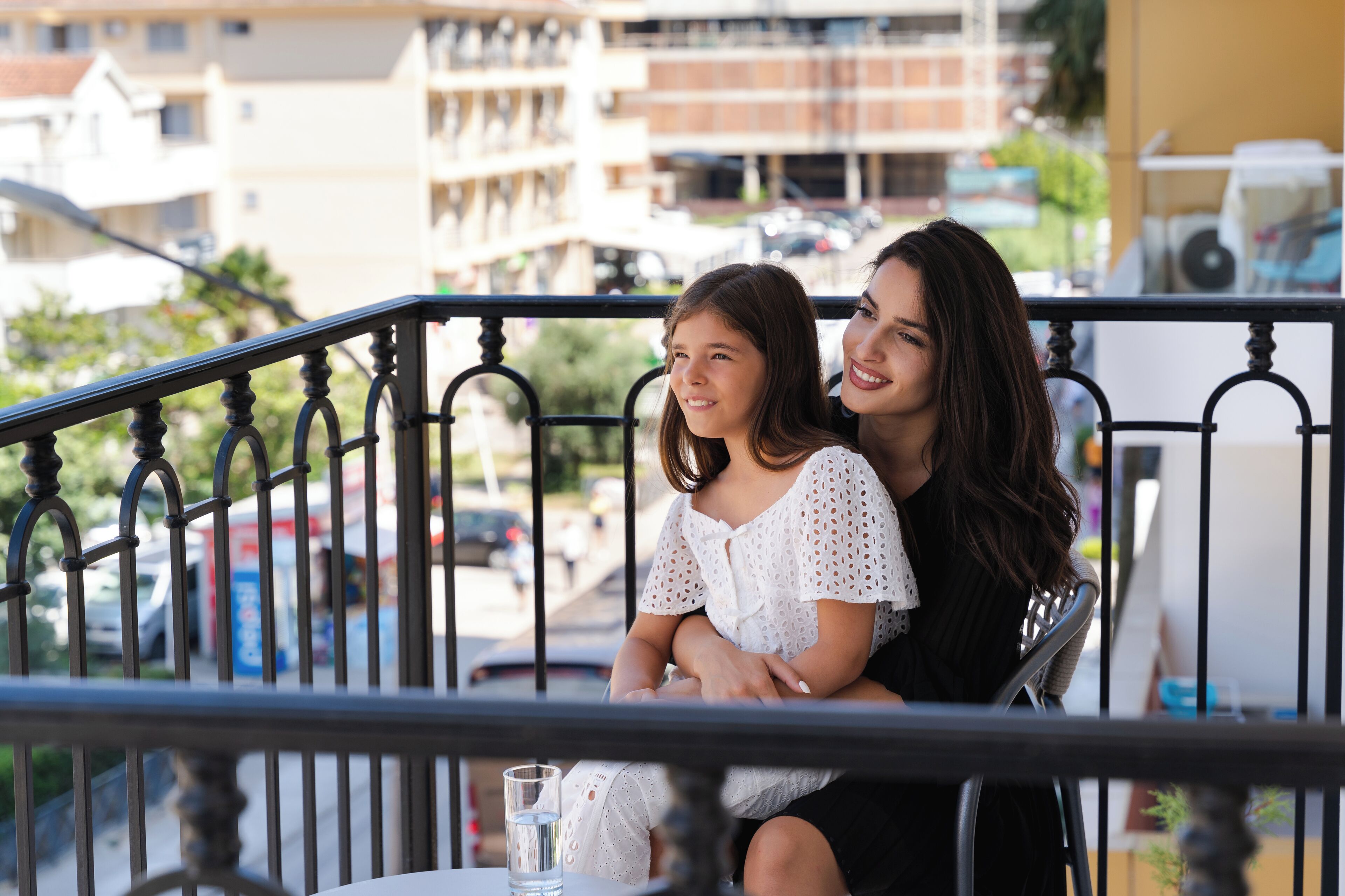 A balcony with a metal railing, a glass table, and a clear view of the street and buildings in the background.