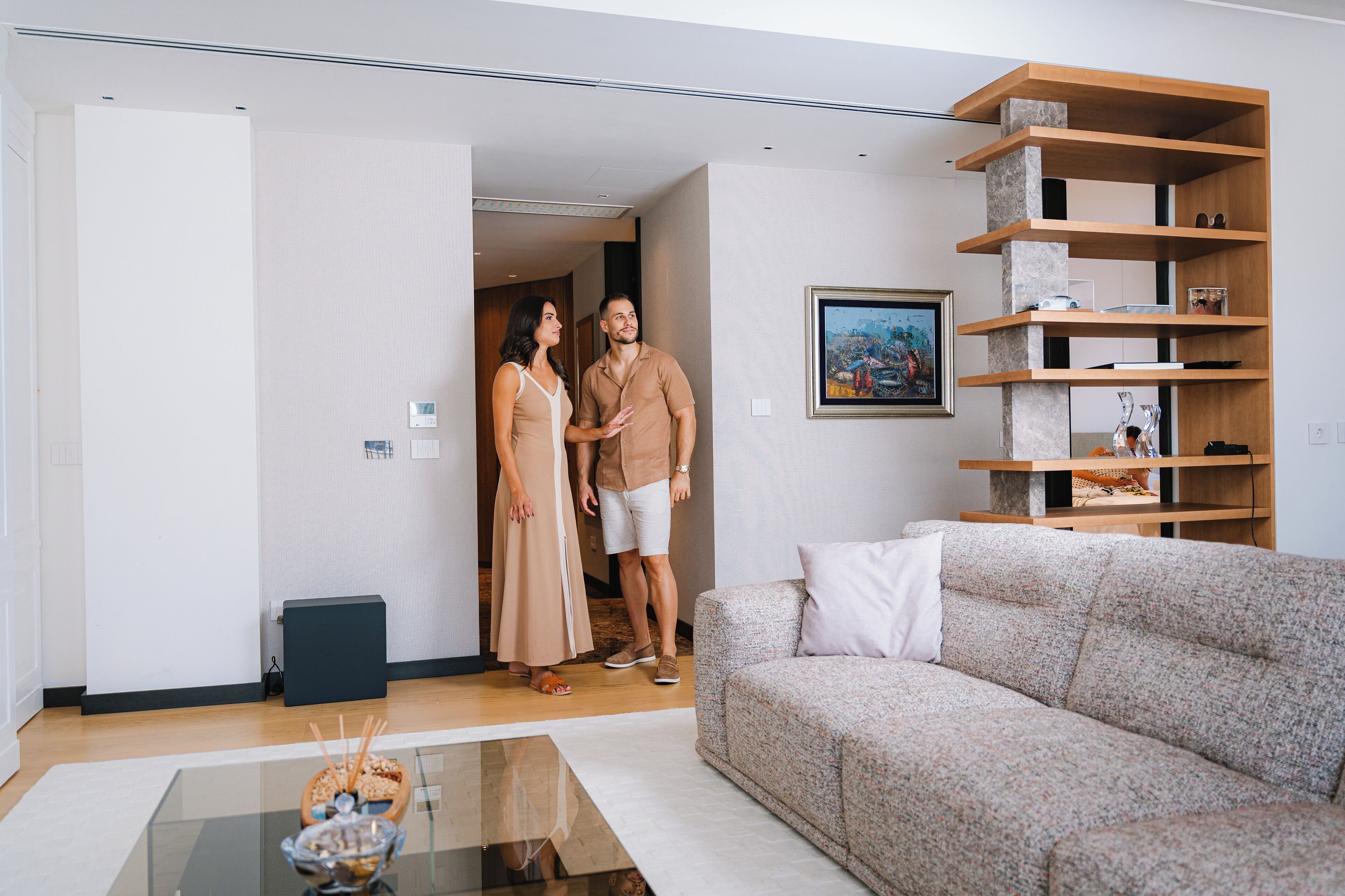 A modern living room with a sofa, a glass coffee table, and a wooden bookshelf.