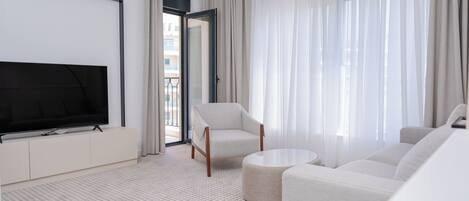 A modern hotel room with a flat-screen TV, a sofa, a chair, and a round coffee table.