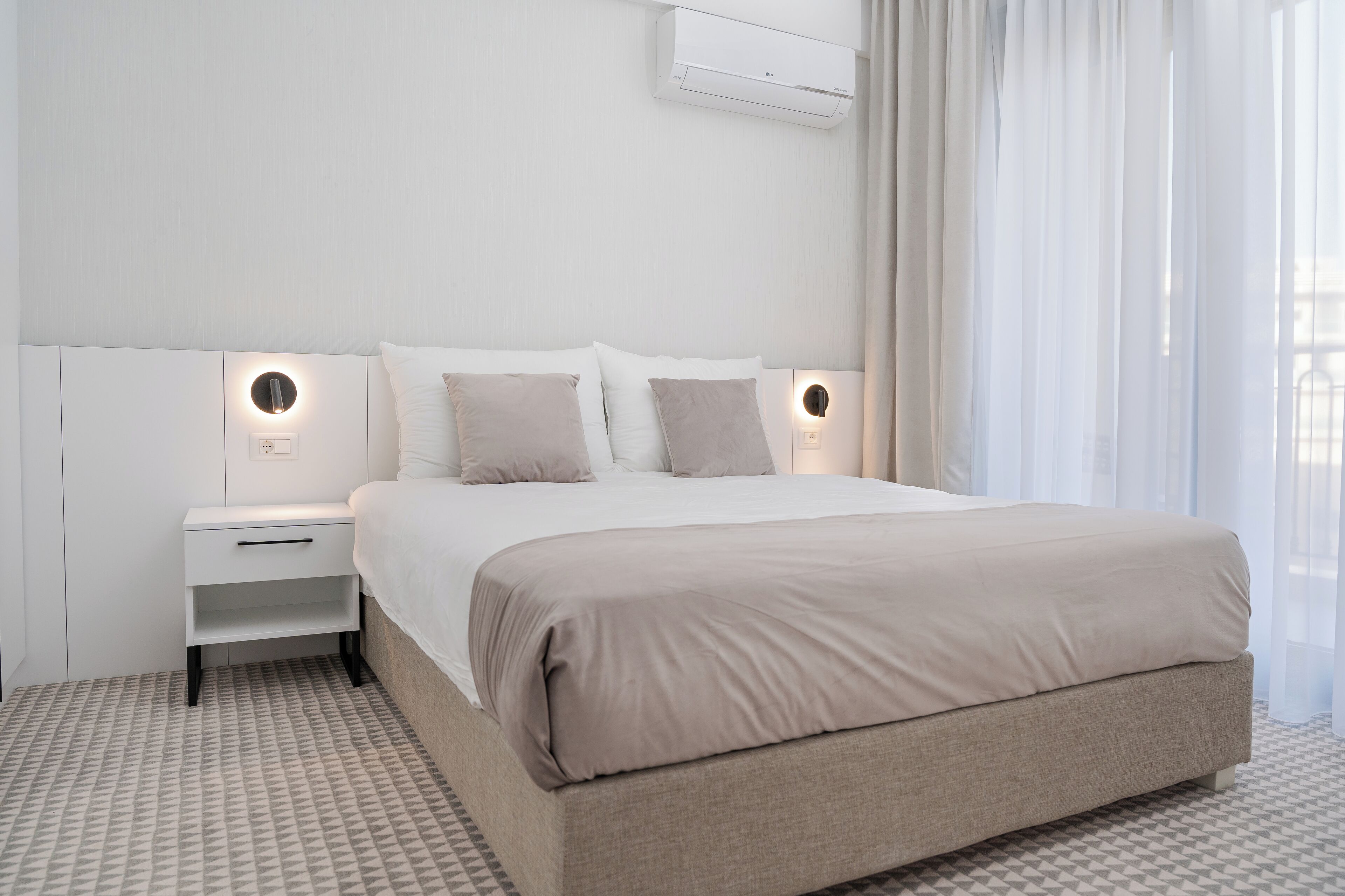 Et moderne hotelværelse med en stor seng, sengeborde og en vægmonteret klimaanlæg.