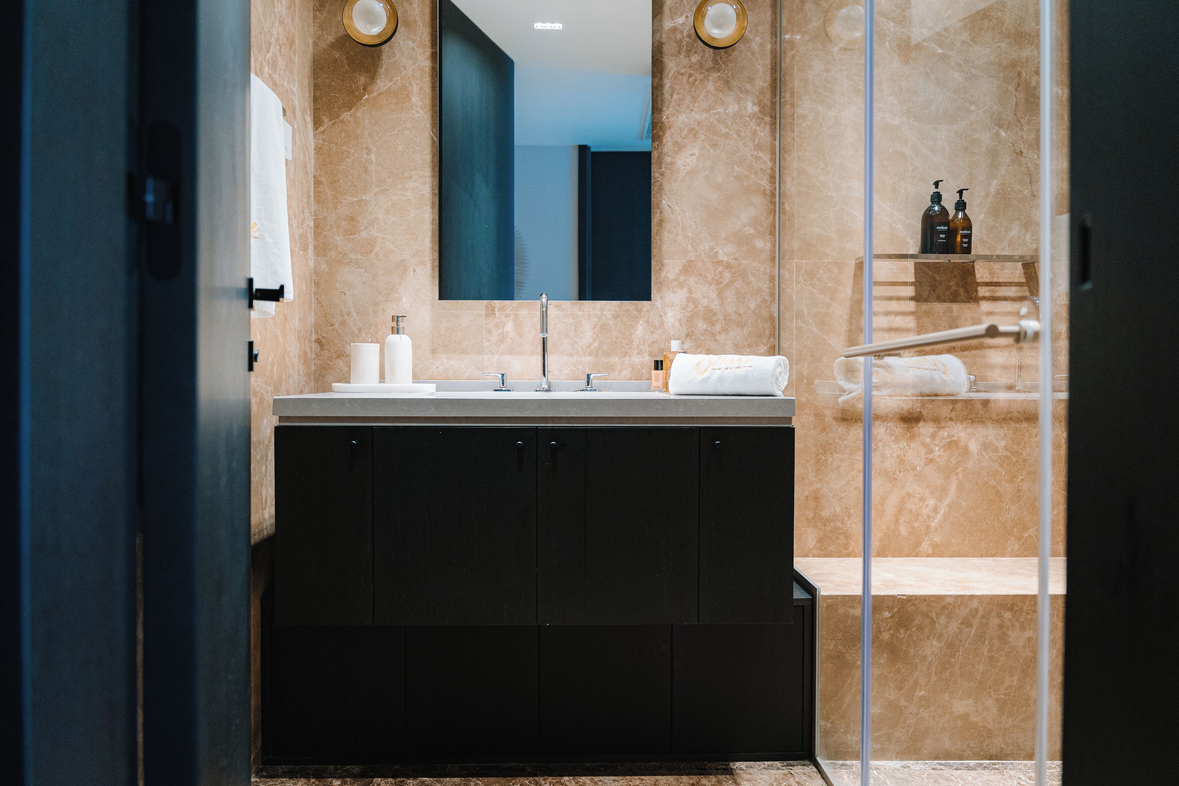 A modern bathroom with a large mirror, dark cabinets, and a glass shower enclosure.
