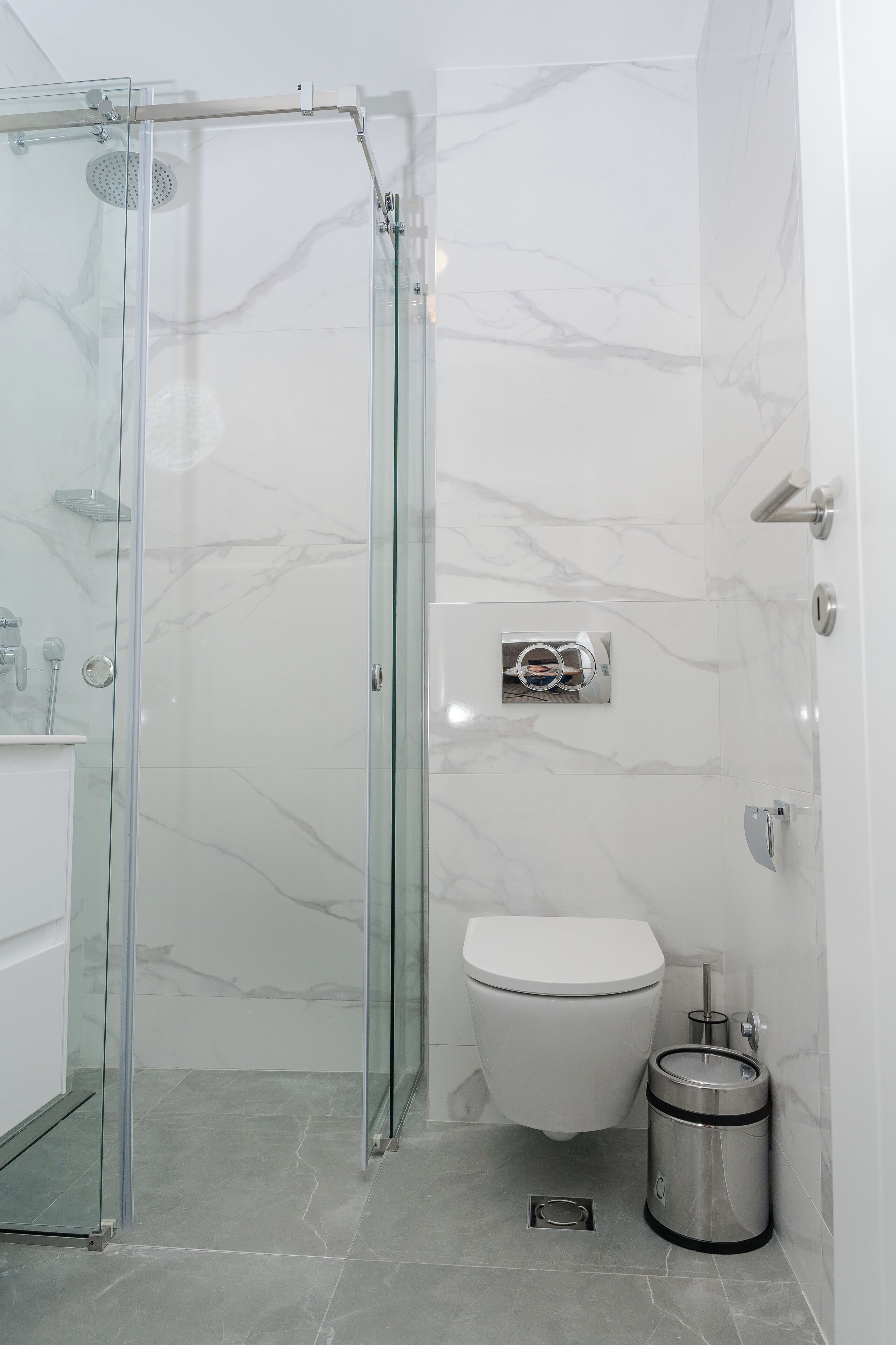 Ein modernes Badezimmer mit einer gläsernen Duschkabine, einer Toilette und einem Mülleimer.