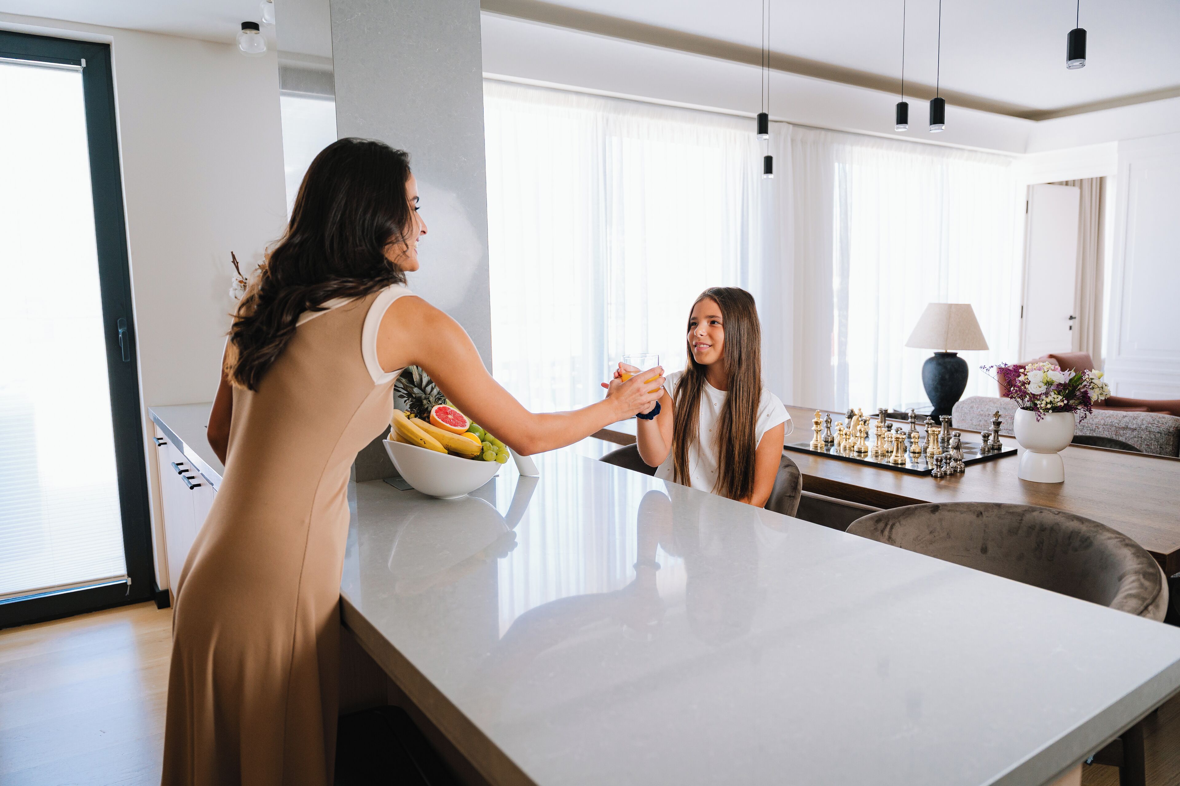 A modern kitchen with a large island, a bowl of fruit, and a chessboard.