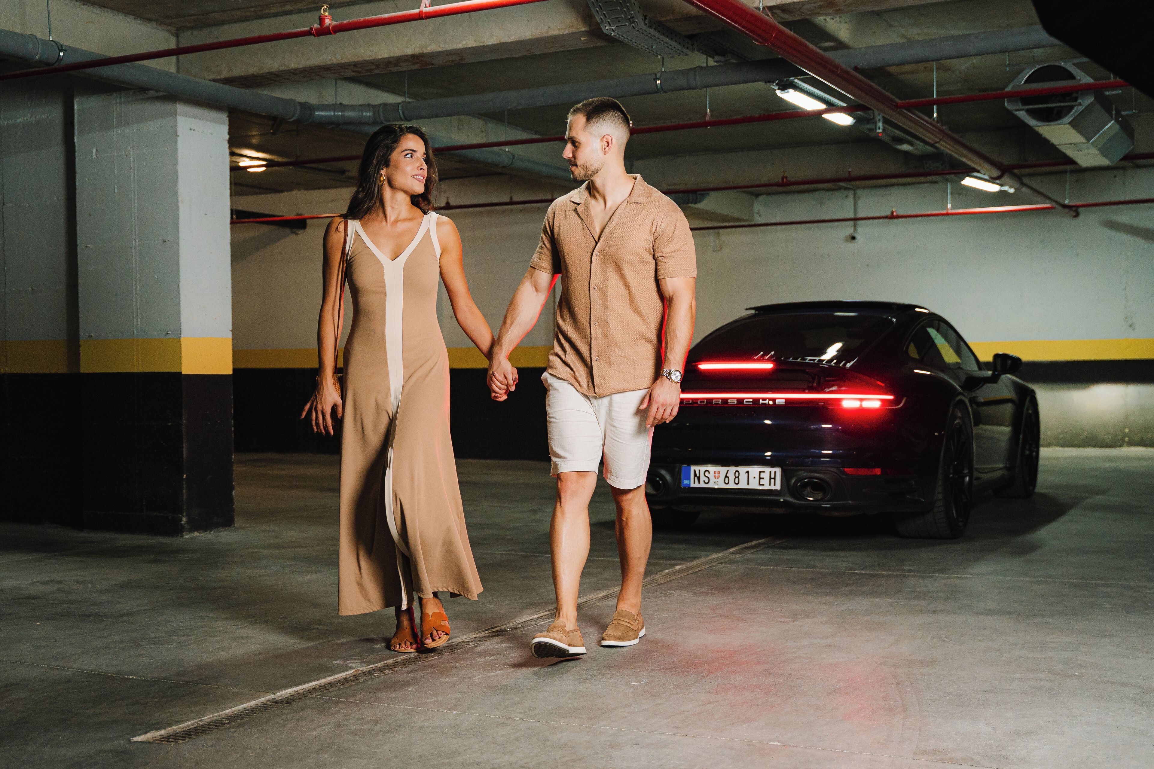 A man and a woman holding hands in a parking garage with a black car in the background.