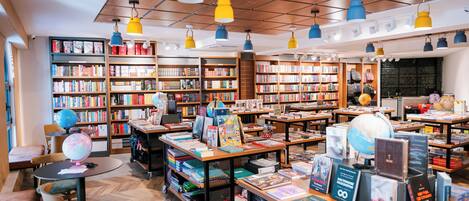 A bookstore with wooden shelves, tables, and chairs, and hanging blue and yellow lamps.