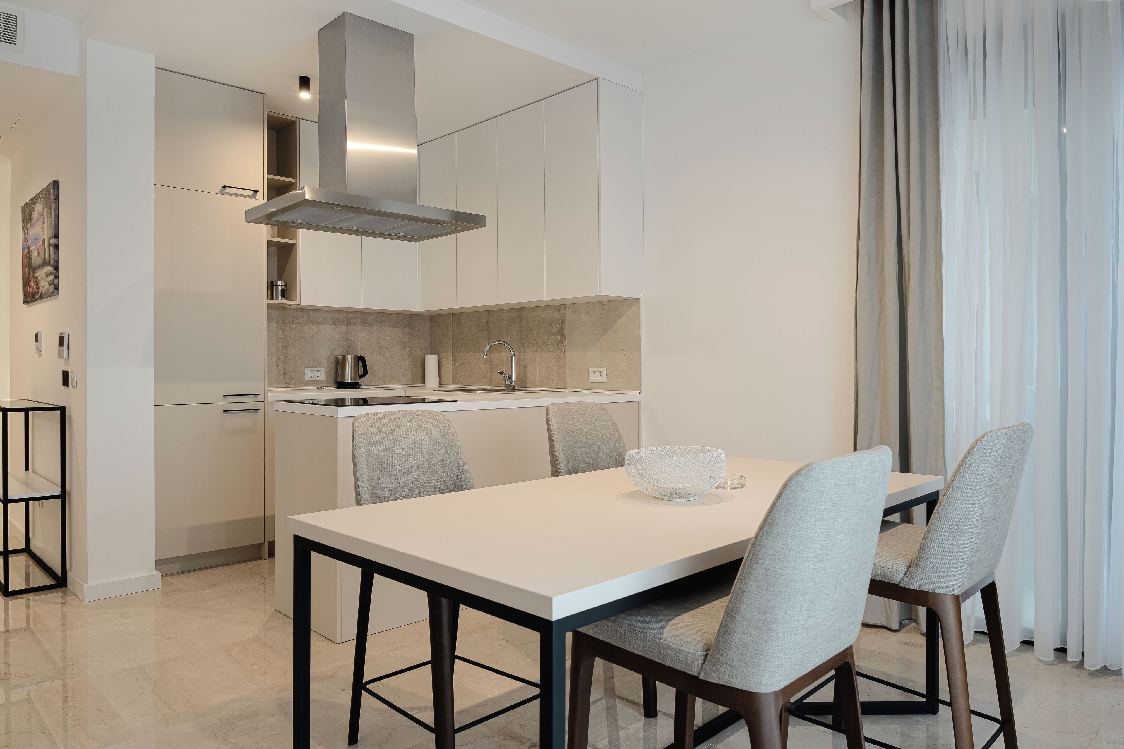 Une cuisine moderne avec un coin repas, comprenant une table blanche, des chaises grises et une hotte de cuisine en acier inoxydable.