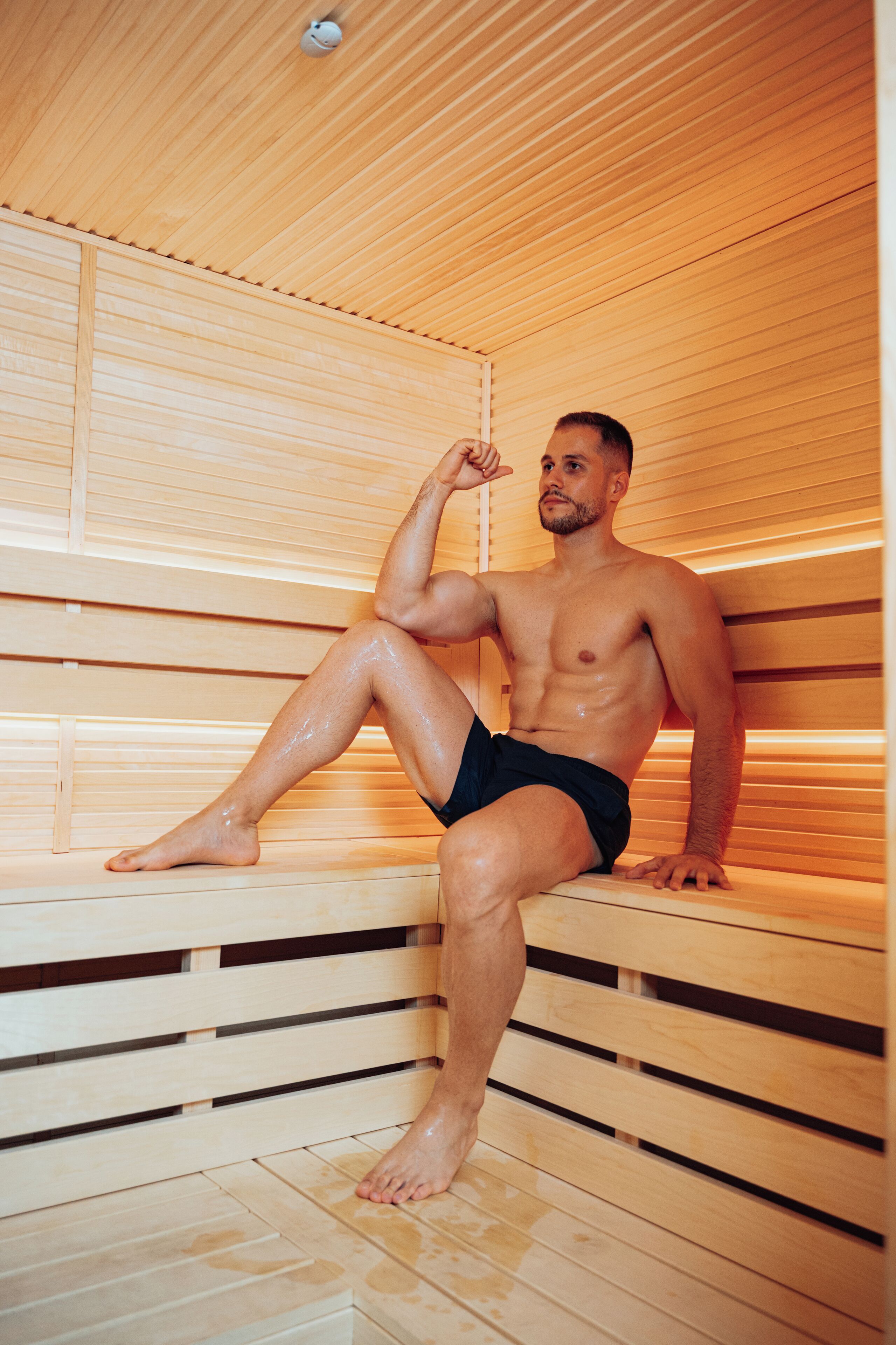 A man sitting in a sauna with wooden benches and slatted walls.
