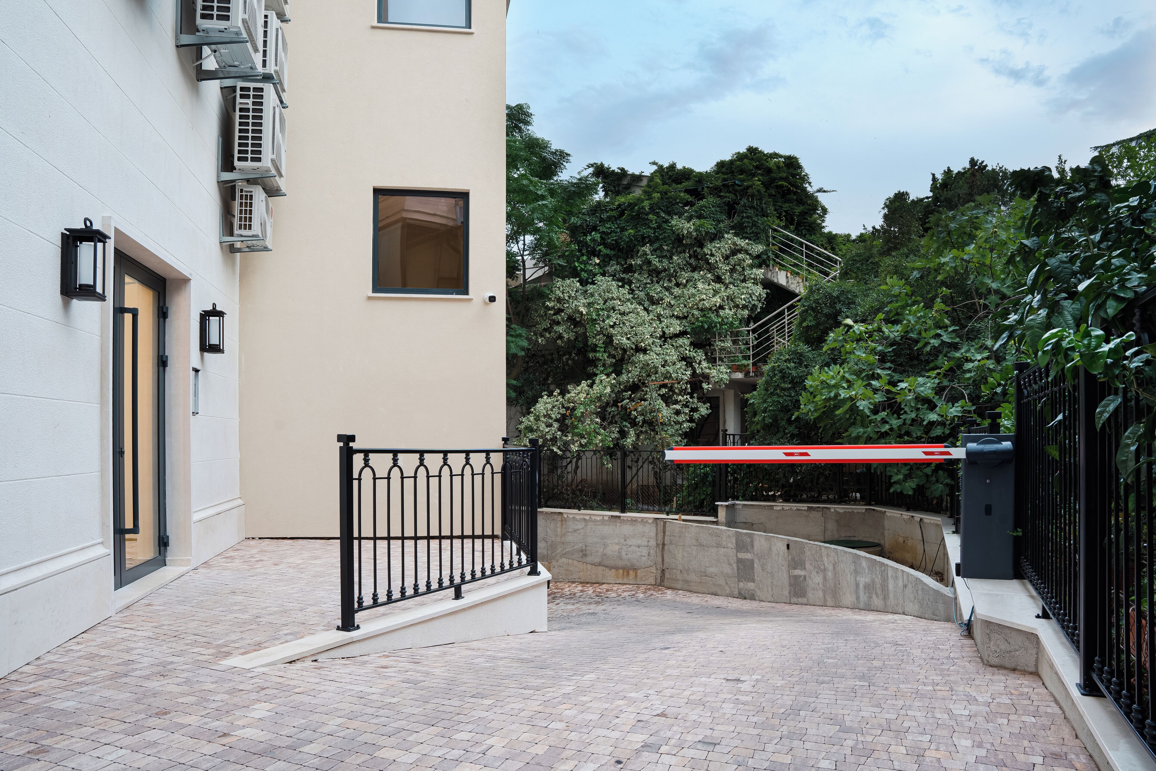 A courtyard with a brick pathway, a black metal railing, and a red and white gate.