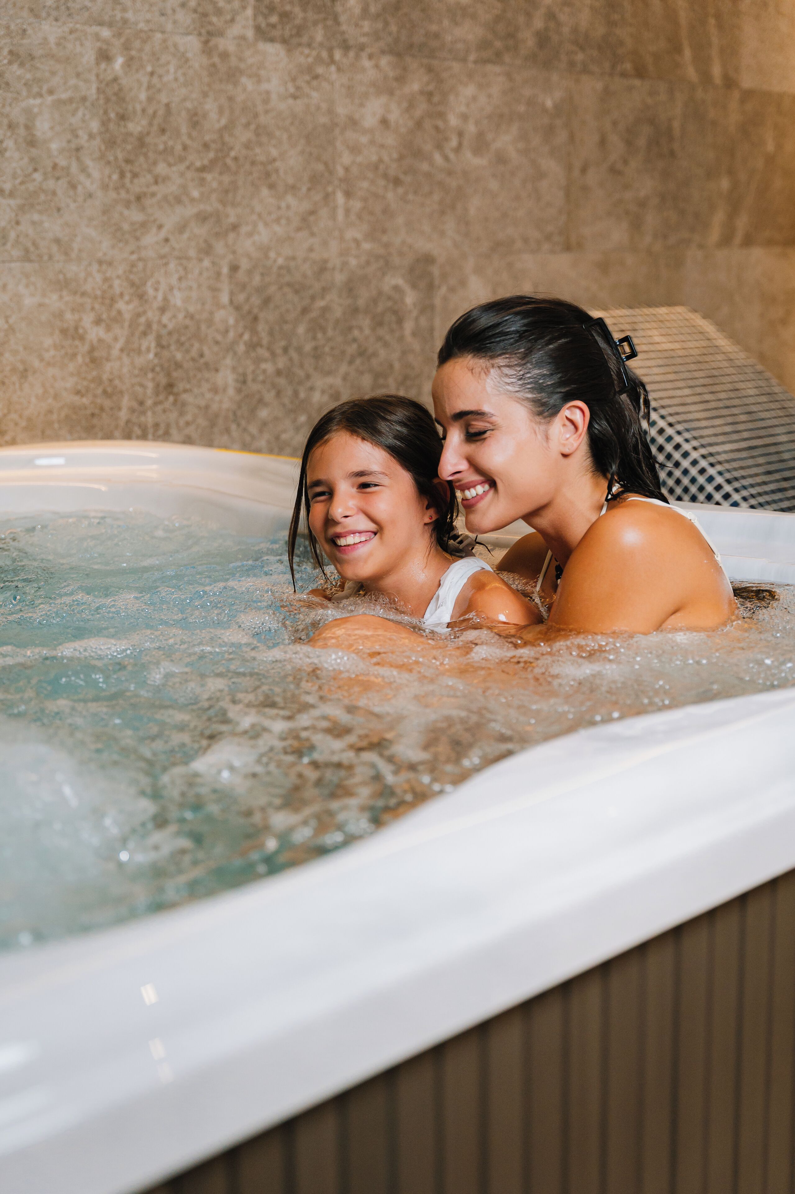 Dos personas en un jacuzzi con una pared de azulejos al fondo.