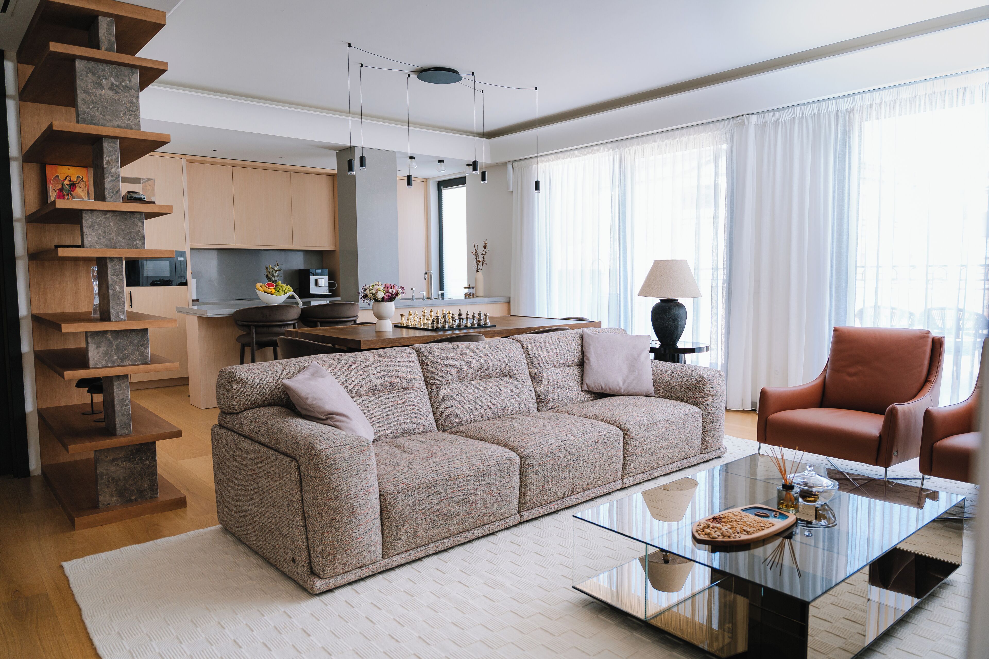 A modern living room with a sofa, a glass coffee table, and a red armchair.