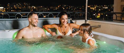Tres personas en un jacuzzi con vistas a un paisaje urbano.