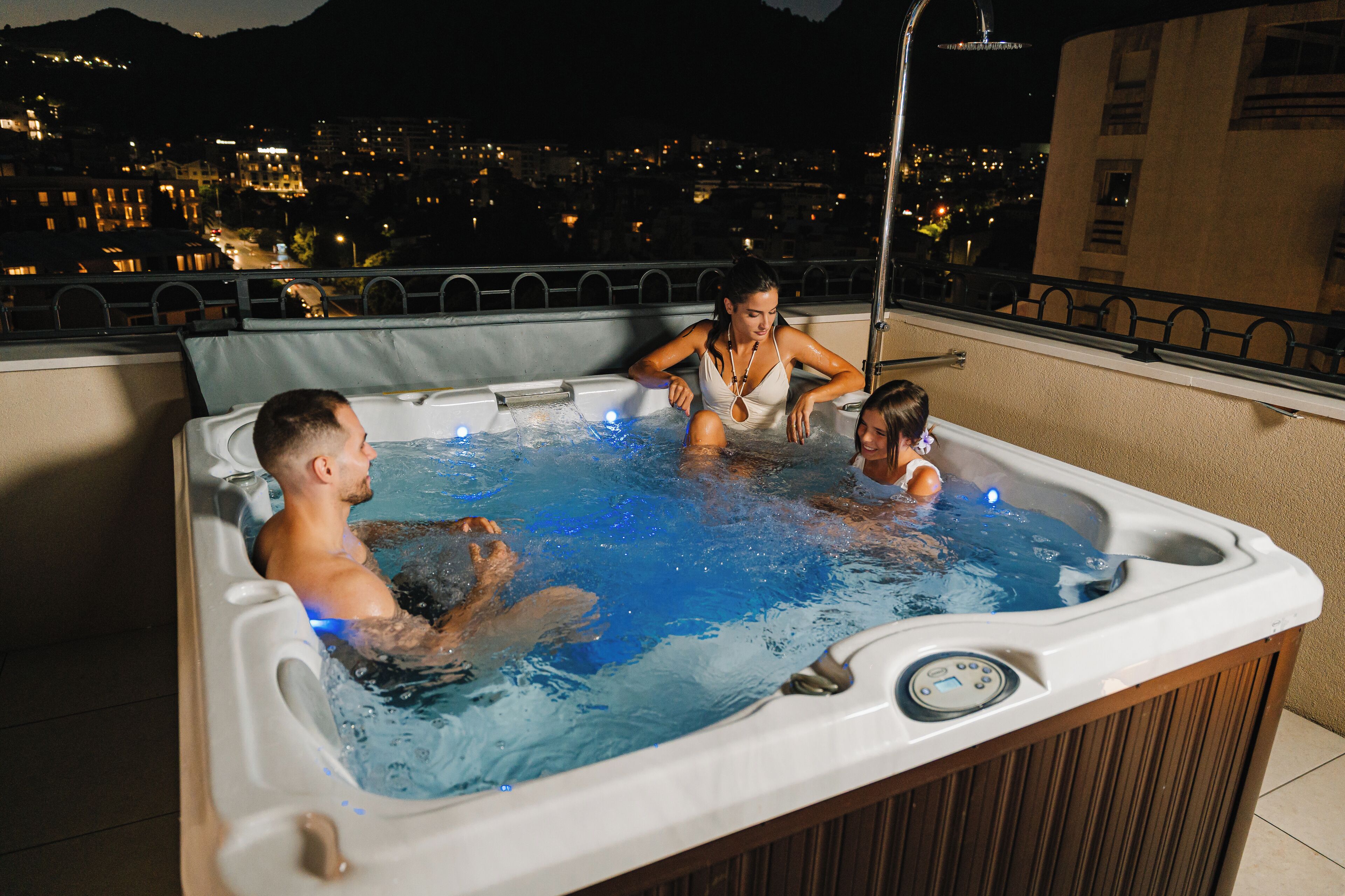 Ein Whirlpool mit drei Personen, Blick auf die Stadtlandschaft und einem Balkongeländer.