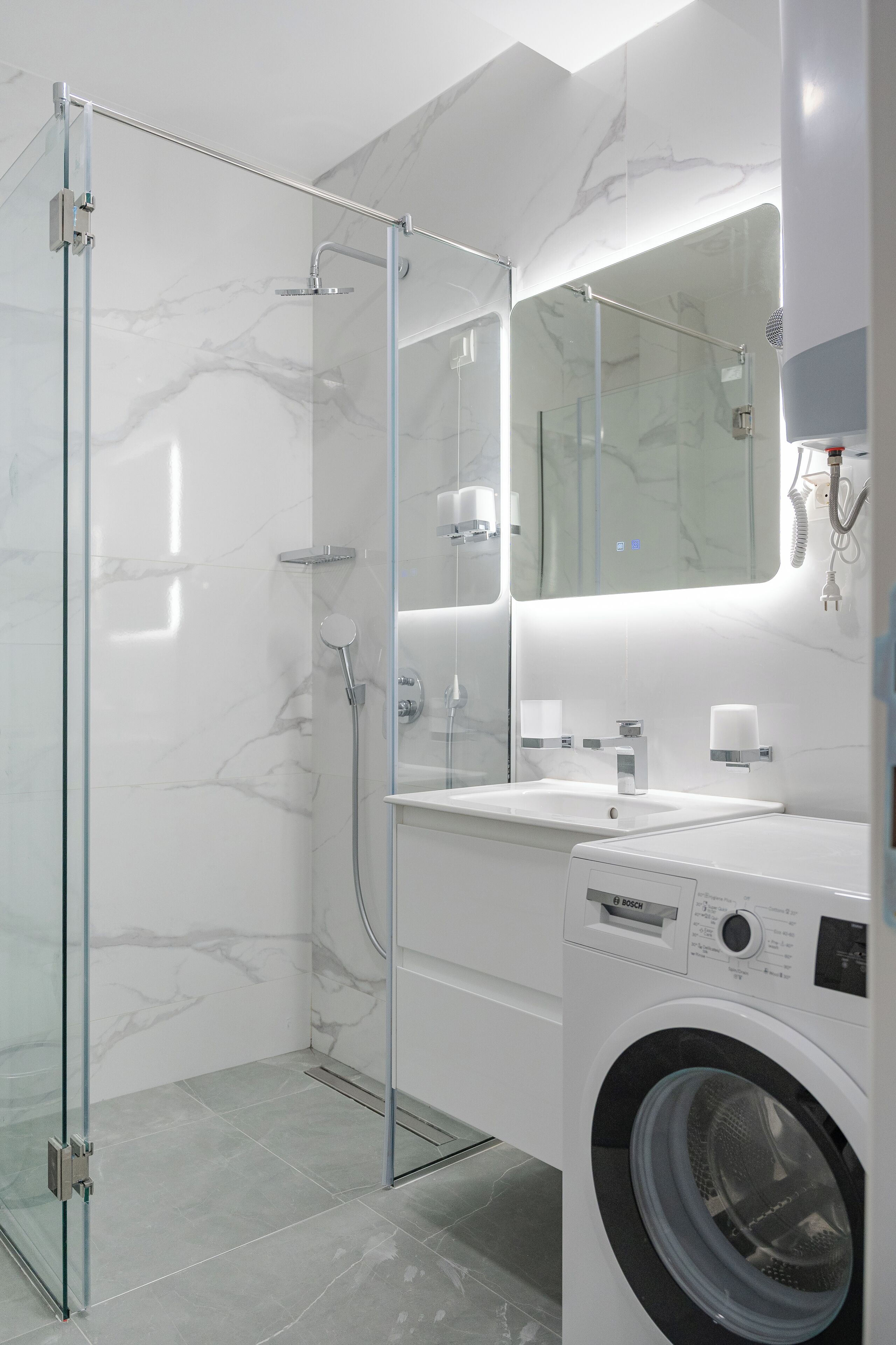 Een moderne badkamer met een douche met glazen wand, een Bosch wasmachine en een grote spiegel.