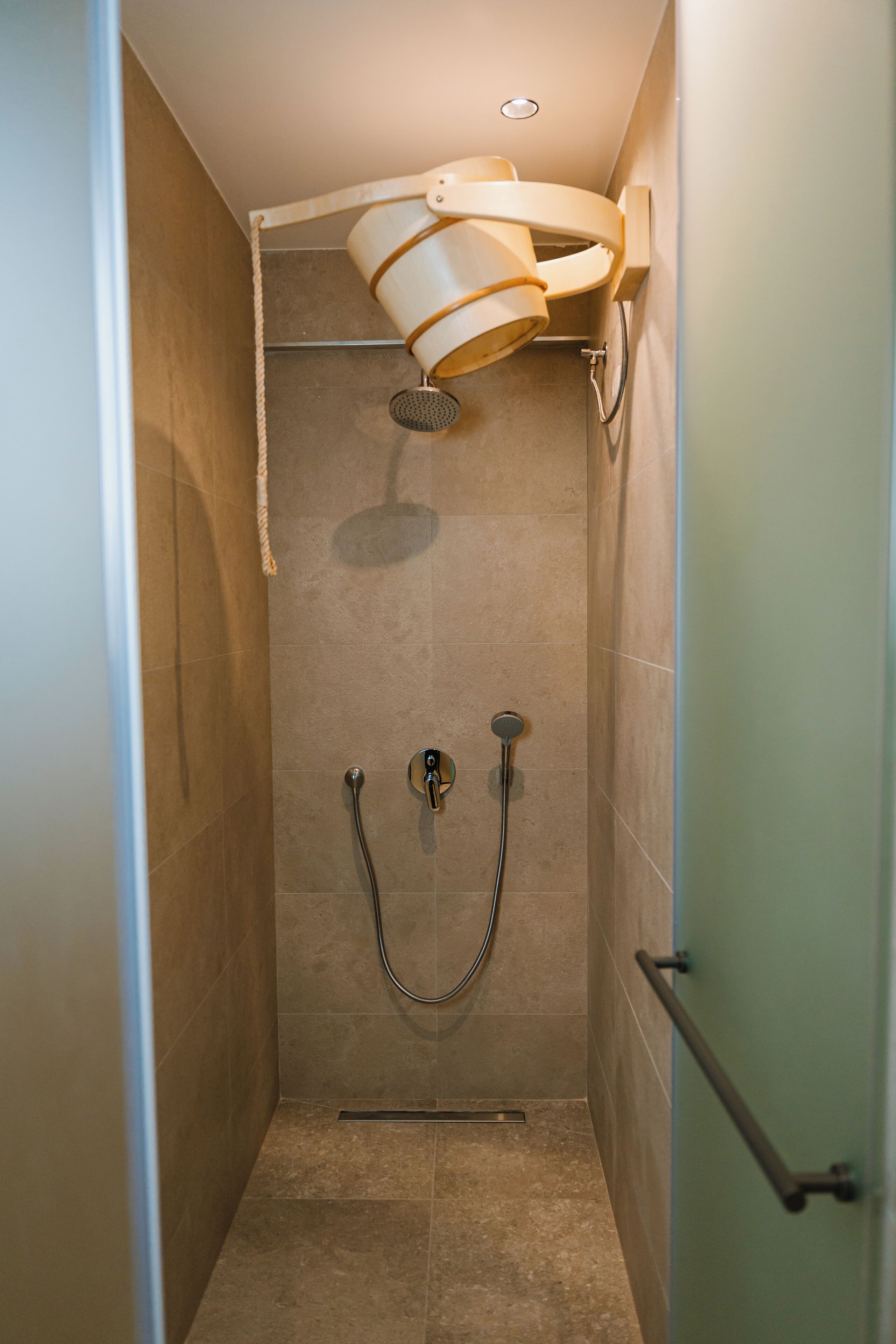 A shower stall with a handheld showerhead, a wall-mounted faucet, and a handheld showerhead.