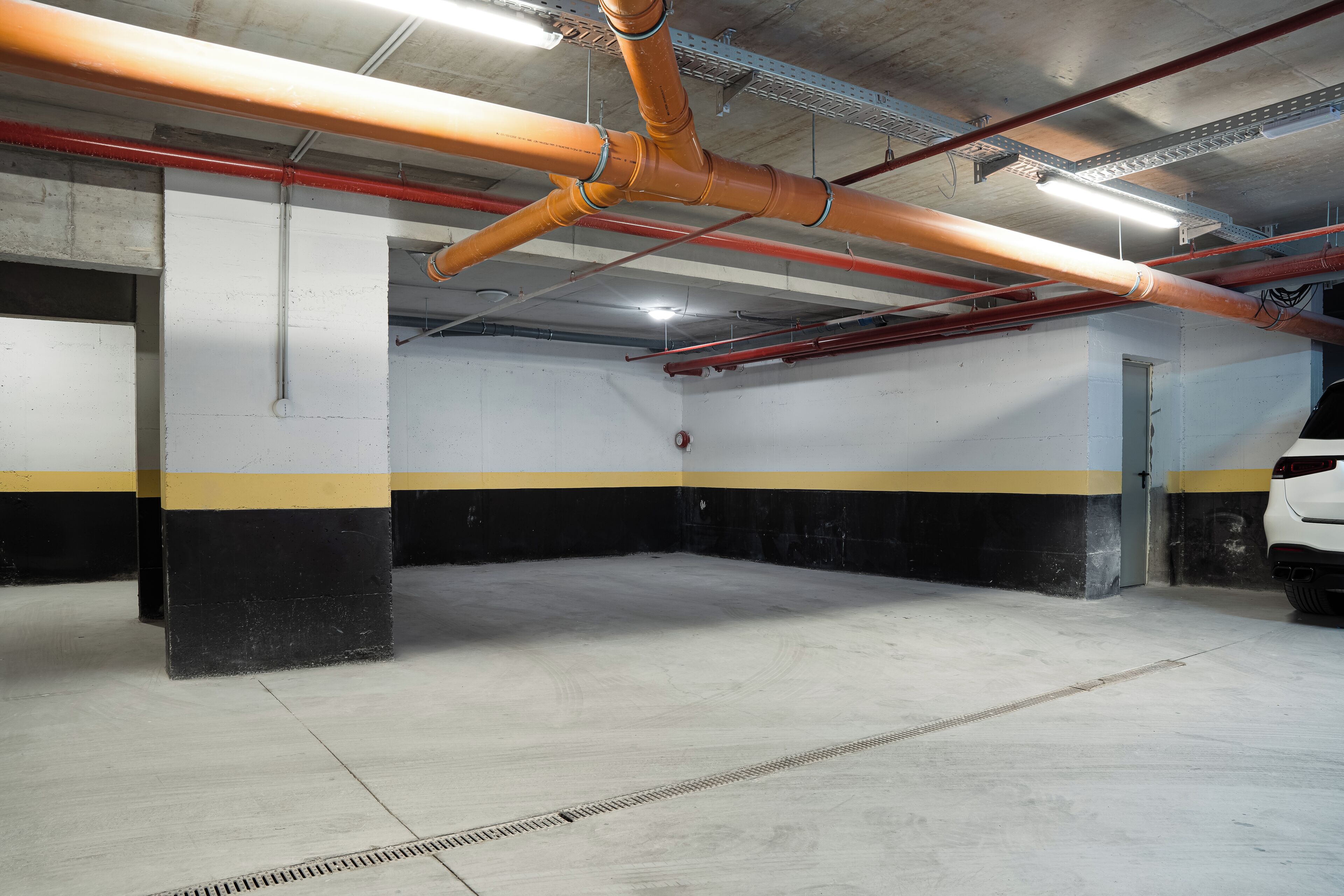 Un garaje para estacionar con pisos de concreto, paredes pintadas de amarillo y negro, y vigas y tuberías estructurales visibles.