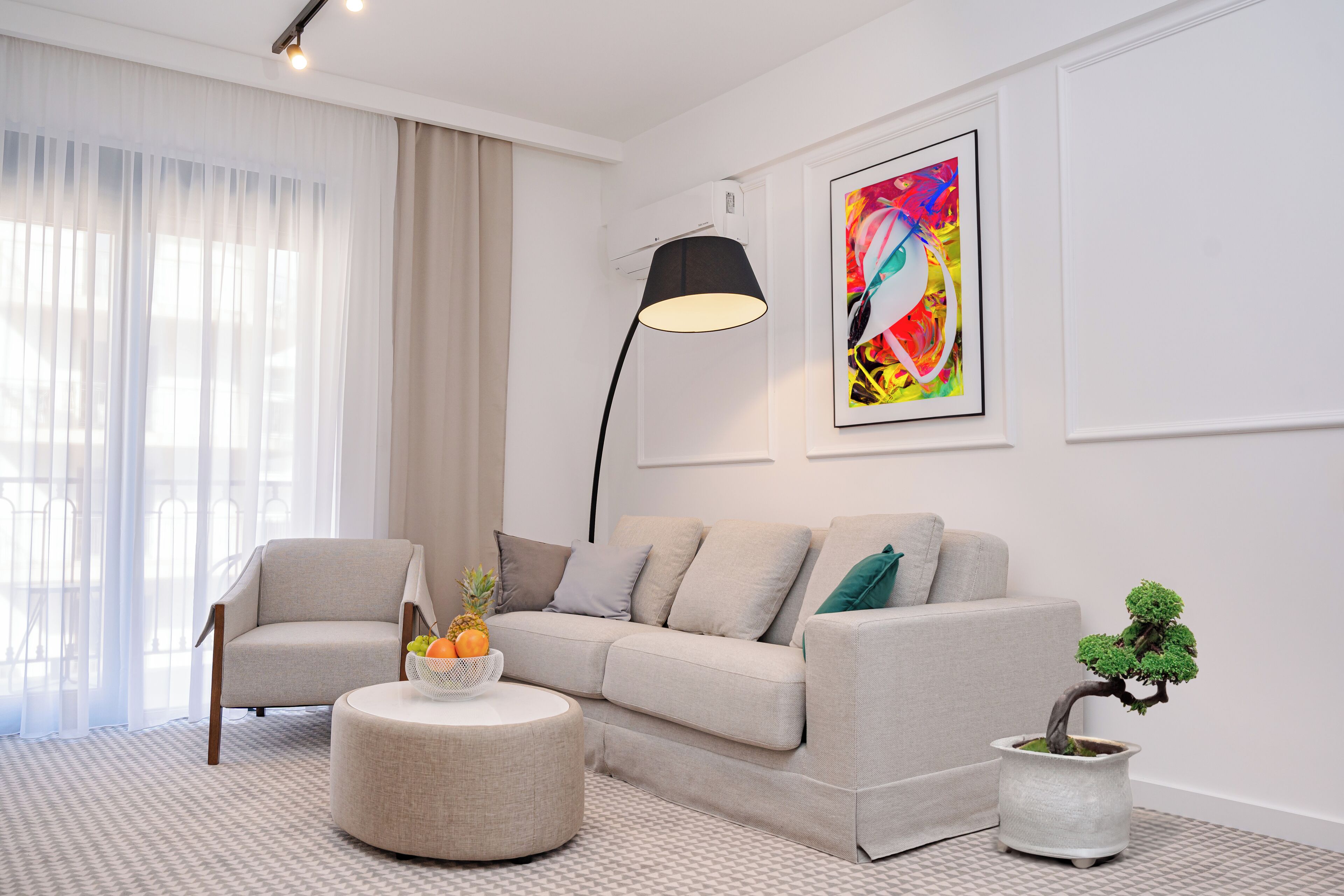 A modern living room with a sofa, armchair, round ottoman, and a potted plant.