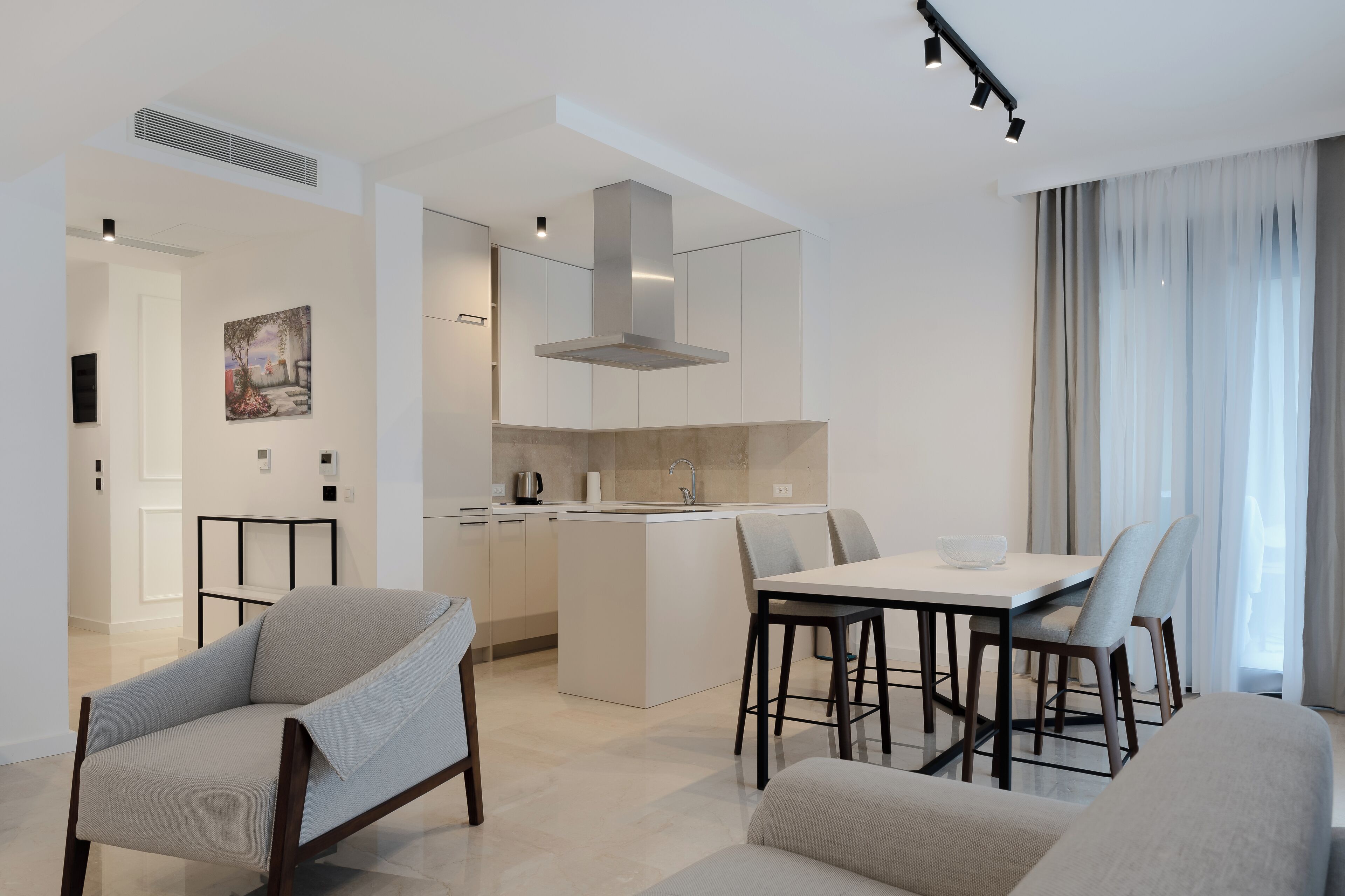 A modern kitchen with a central island, dining area with chairs, and a living space with sofas.