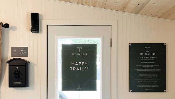 Een hotelkamerdeur met een bord waarop 'Happy Trails!' staat, een sleutelpost en een bord met informatie over faciliteiten.